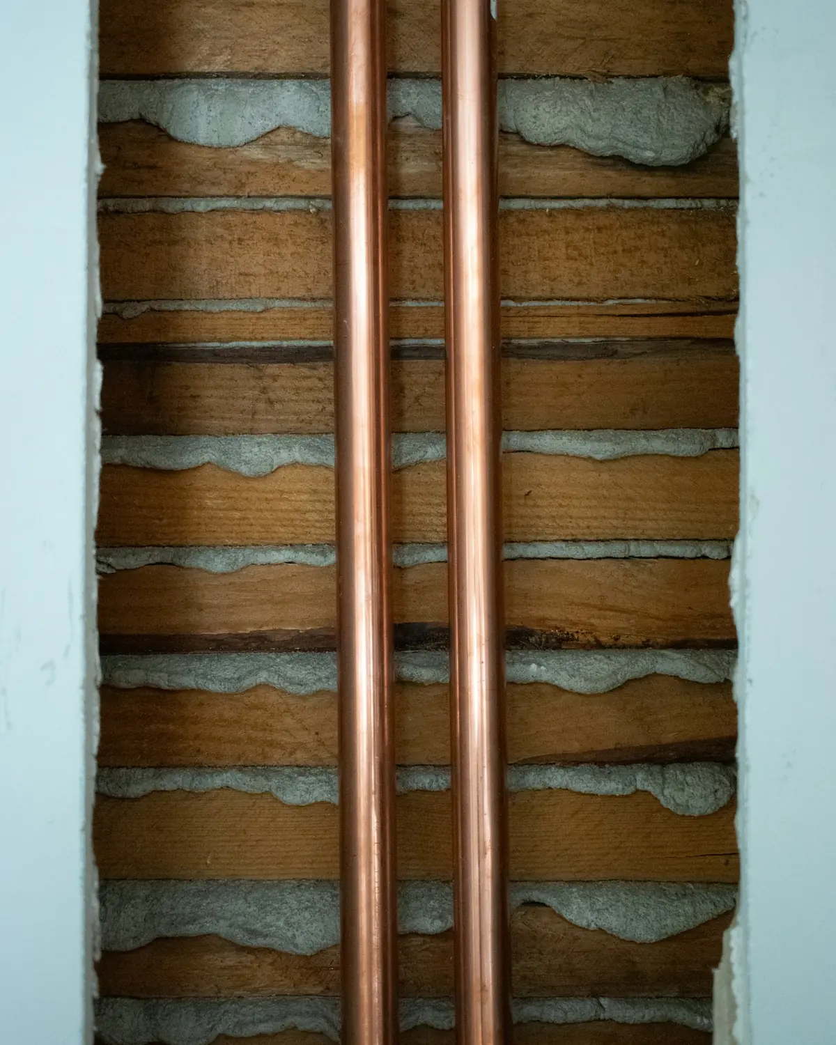 Two copper pipes running up a timber wall.